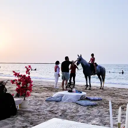 Child riding a horse on the beach with family and trainers assisting at Al Jazeerah Equestrian Club.