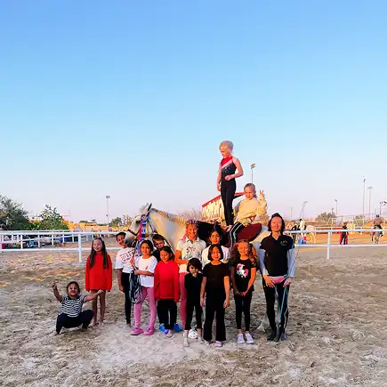 Group of children posing with a horse and instructor during a riding activity at Al Jazeerah Equestrian Club.