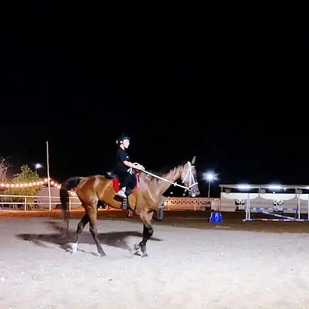 A young rider practicing horse riding at night under arena lights at Al Jazeerah Equestrian Club.